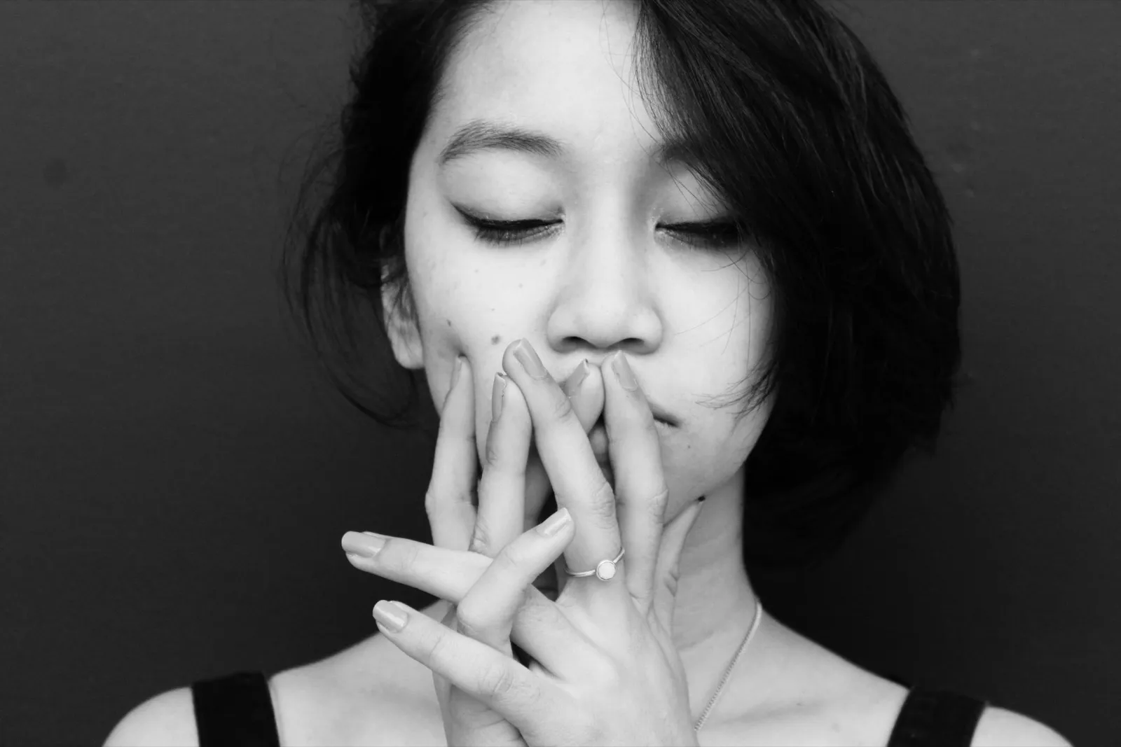 Femme les yeux fermés, les mains devant la bouche, en noir et blanc