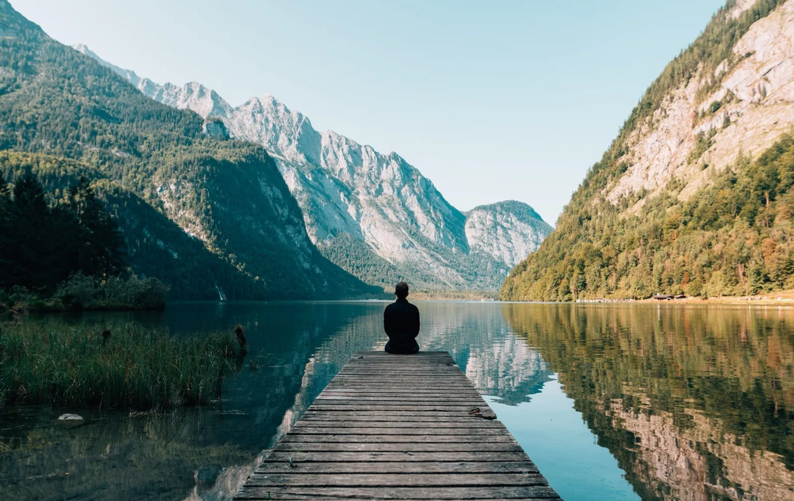 Personne assise au bout d’un ponton face à un lac de montagne